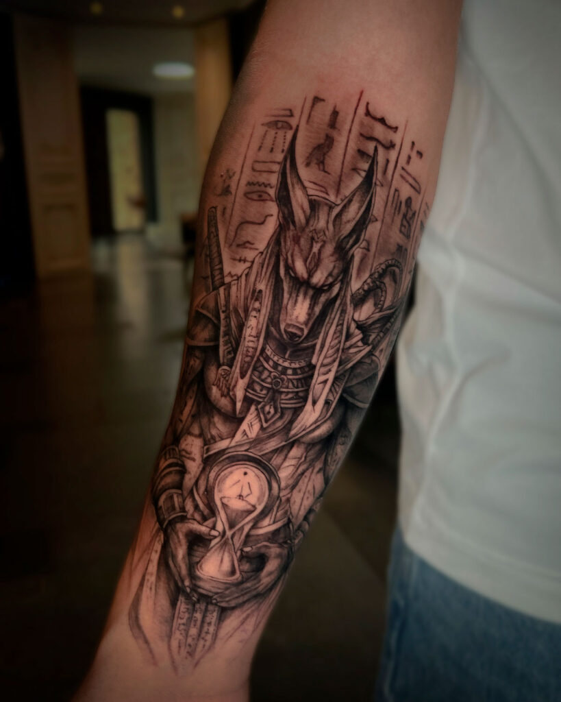 Tatuaje de anubis con un reloj de arena, en antebrazo, tatuado por kaorukel