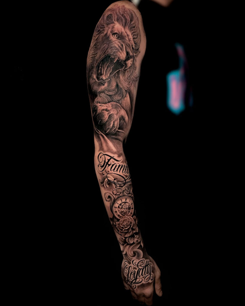 Tatuaje en brazo completo de un leon, la palabra familia, un reloj, una rosa y la palabra lealtad en la mano, estilo realismo, tatuado por kaorukel