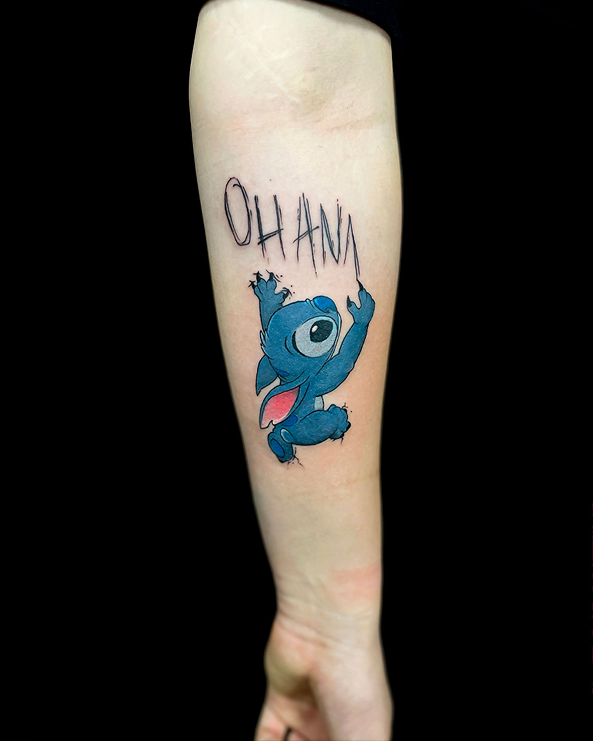 Tatuaje de Stitch, personaje de animación, rascando la palabra ohana en la piel, tatuado por kaorukel